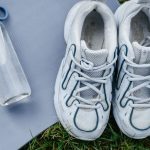 Top view of white sneakers and water bottle placed on a yoga mat outdoors.