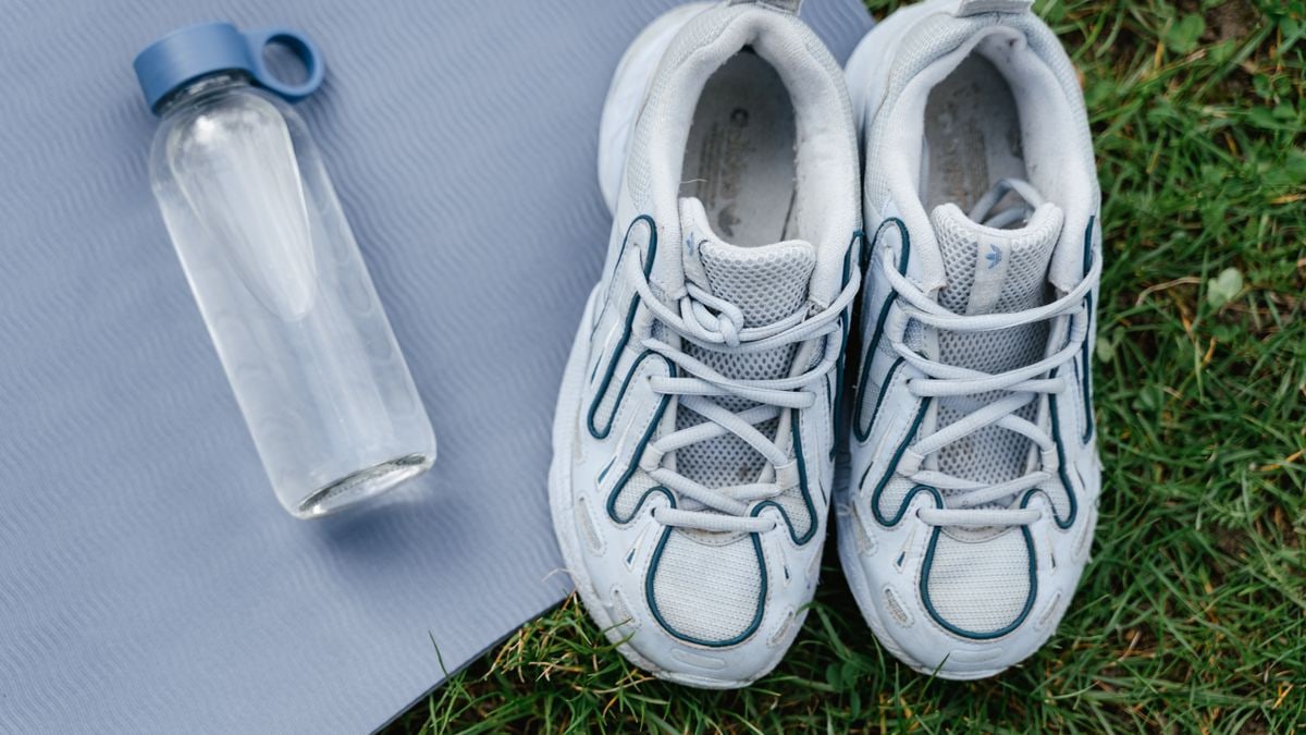 Top view of white sneakers and water bottle placed on a yoga mat outdoors.